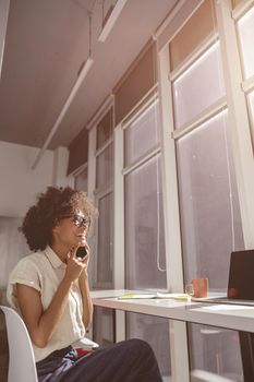 Smiling Afro American female worker sitting at workplace in coworking while using smartphone during sunny day