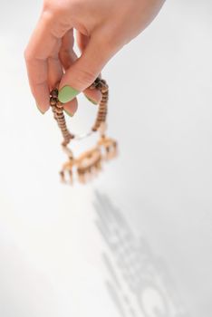 Woman’s hand with green manicure holding wooden handcraft necklace. Shadow on a white background.