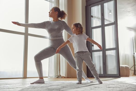 Low angle of calm mother doing asana while little girl is assisting her in living room
