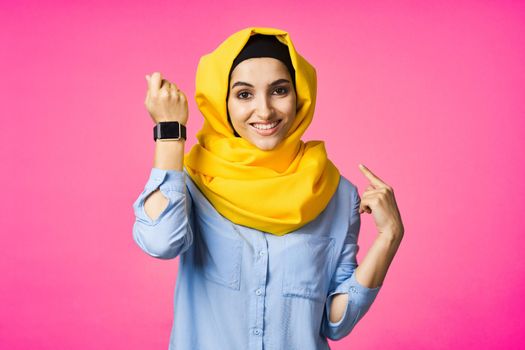 cheerful woman in yellow hijab electronic watch technology user pink background. High quality photo