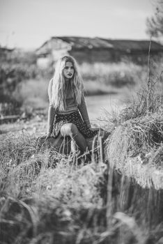 Beautiful young blonde woman, model of fashion, in rural background. Girl wearing sweater and skirt. Black and whit shoot.