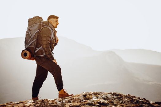 Male backpacker or hiker in hiking equipment standing at the top of the mountain
