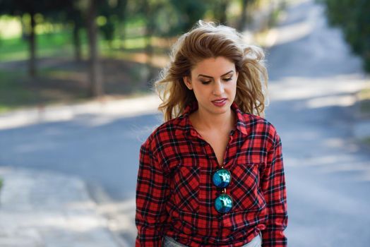 Beautiful sad young woman in the park. Girl with long blonde curly hair.