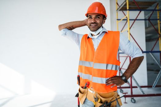 Portrait of mixed race man builder in workwear and hardhat wearing medical mask, close up photo
