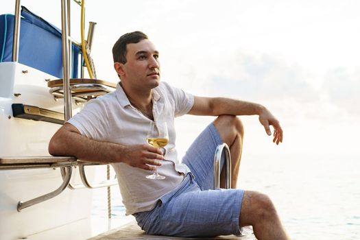 Young man holding a glass of wine on an open deck of a cruise boat, close up
