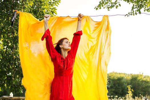 woman in a red dress with hands raised up yellow fabric nature. High quality photo