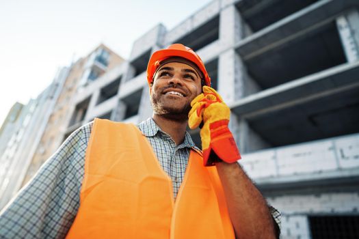Young construction worker in uniform using walkie talkie on site, close up portrait