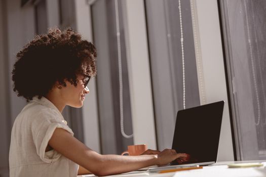 Smiling female assistance sitting at workplace while typing on laptop near the window