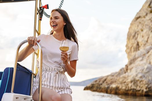 Young woman holding a wineglass and sitting on deck of sailing yacht boat