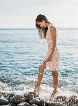 Beautiful young woman walking on pebble beach near the sea