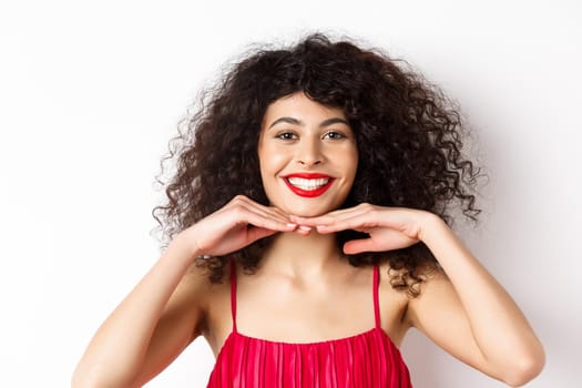 Beauty and makeup. Pretty lady with curly hair, red lips and white teeth, smiling and showing perfect face, standing on white background.