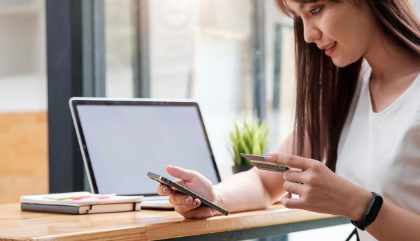 Online shopping concept, young woman hands holding using mobile smart phone and credit card making online payment with laptop computer on table while holiday.