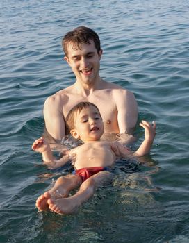 Happy family and healthy lifestyle. A young father teaches a child to swim in the sea