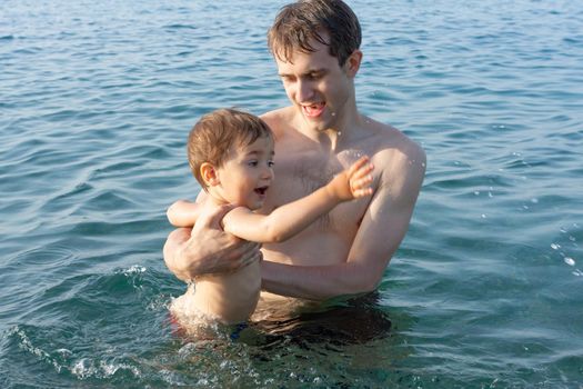 Happy family and healthy lifestyle. A young father teaches a child to swim in the sea