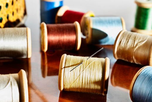 Spools of colored thread and needle on wooden table ,in the background sewing basket