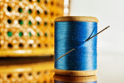 Spool of blue thread and one needle on wooden table ,in the background sewing basket