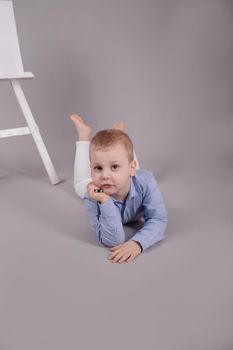 preschool blonde boy in white pants and blue shirt on grey background. child, kid isolated.