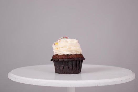 tasty chocolate cupcake with white topping cream on a white stand on a gray background. sweets, bakery. party food. dessert.