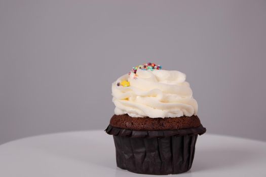 tasty chocolate cupcake with white topping cream on a white stand on a gray background. sweets, bakery. party food. dessert.