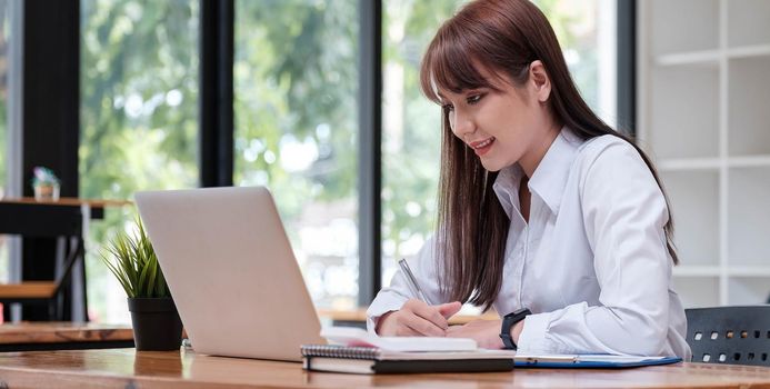 Asian young businesswoman sitting and happy working with laptop computer connect internet in desk office.