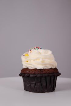 tasty chocolate cupcake with white topping cream on a white stand on a gray background. sweets, bakery. party food. dessert.