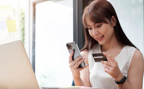 Portrait of a happy woman buying online with a smart phone in office..