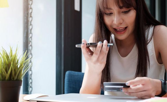 Smiling female having phone conversation while working on laptop and paying for purchases with credit card in cafe.