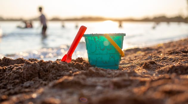 Children's toys for playing on the sand. Plastic bucket and rake on the beach at sunset. The concept of summer, family holidays and vacations.