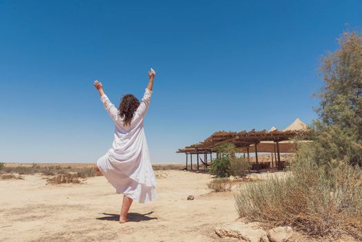 A woman stands in the desert and looks at the horizon. White clothing fluttering in the wind. Concept for relaxation, inner looking, meditation, peace of mind. High quality photo