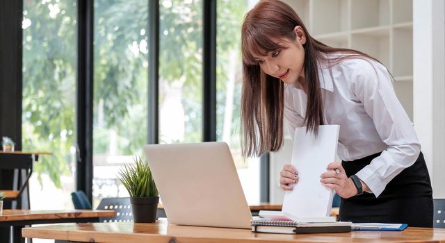 Smart businesswoman analyzing business data, reviewing profits report and working on laptop computer with calculator on desk in office, startup business, business strategy analysis concept, close up.