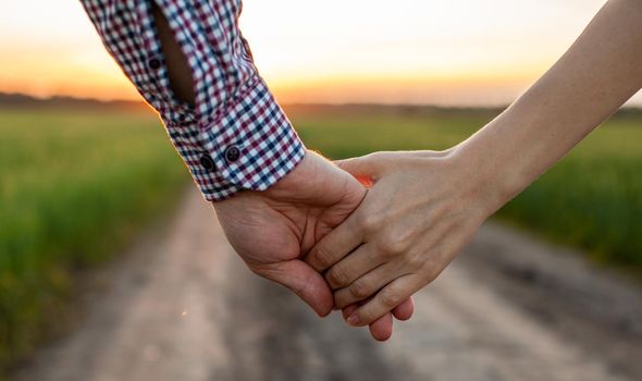 Love concept. A couple holding hand during sunset, a symbol of love and happy relationship. A young couple in love walks through a field at sunset, holding hands and looking at the sunset