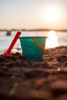 Children's toys for playing on the sand. Plastic bucket and rake on the beach at sunset. The concept of summer, family holidays and vacations.