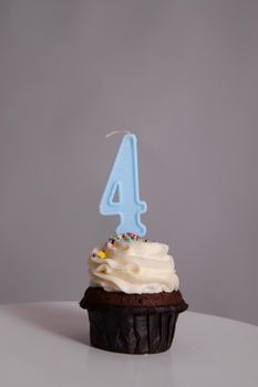 tasty chocolate cupcake with white topping cream and candle in shape of number four 4. on a white stand on a gray background. sweets, bakery. party food. dessert.