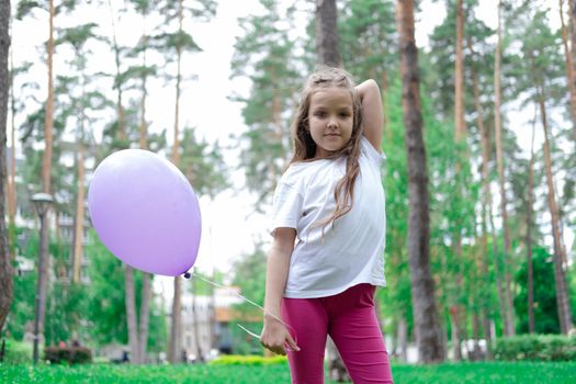 pretty girl in pink leggings and white t-shirt with purple hot air balloon in park. holliday, party, birthday, celebration. happy children.