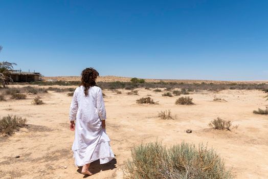 A woman stands in the desert and looks at the horizon. White clothing fluttering in the wind. Concept for relaxation, inner looking, meditation, peace of mind. High quality photo