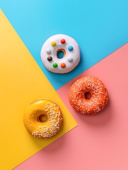 Creative layout made from delicious glazed donuts. Vertical flat lay - donuts or doughnuts on colorful background with copy space. Blue, yellow and pink geometric background.