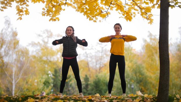 Acrobatic girls in jackets warming up outside before training in park. Hands to the sides. Autumn
