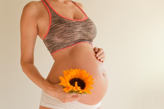 pregnant girl hugs her belly and holds yellow sunflower in her hand. belly skin treatment and maternity