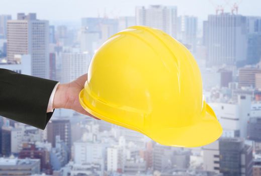 hand of engineer holding yellow helmet with city background
