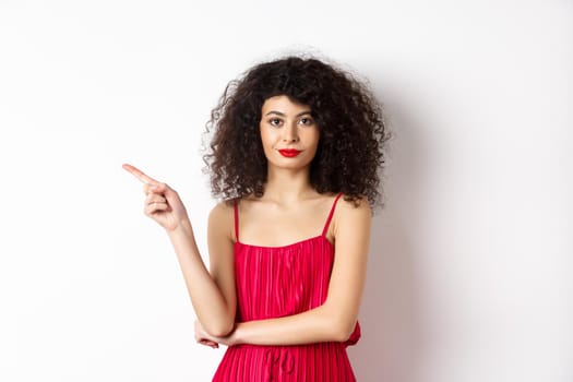 Attractive lady in red dress and makeup pointing finger left, showing logo, standing over white background.