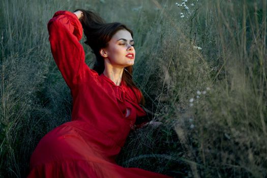 pretty woman in red dress lies on the grass nature sun. High quality photo