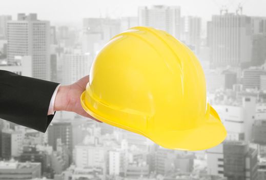 hand of engineer holding yellow helmet with city background