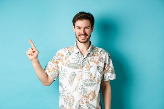 Smiling tourist in hawaiian shirt pointing finger at empty space, showing logo. Concept of vacation and travelling.