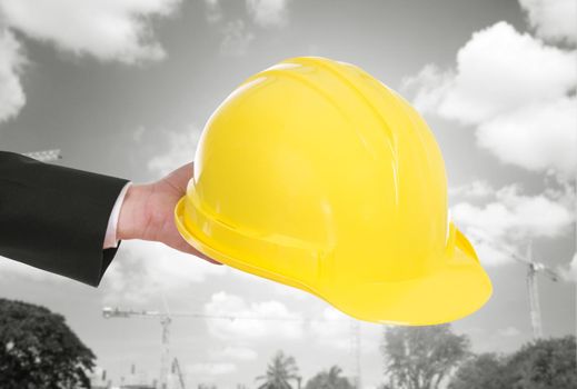 hand of engineer holding yellow helmet with construction crane background