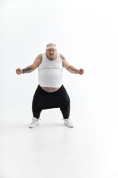 Happy fat man with big belly and tattoes in sports wear posing on white background