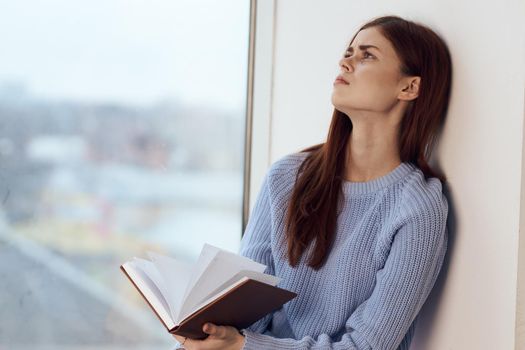 woman reading a book near the window with a cup of drink rest. High quality photo