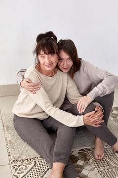 High angle of happy young woman and middle aged mother in comfy casual outfits embracing and looking at camera