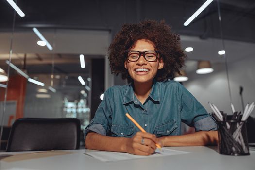 Happy businesswoman in glasses sitting at workplace and working with documents in the office