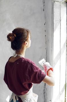 Woman in a white apron paints a window in a house interior renovation. High quality photo