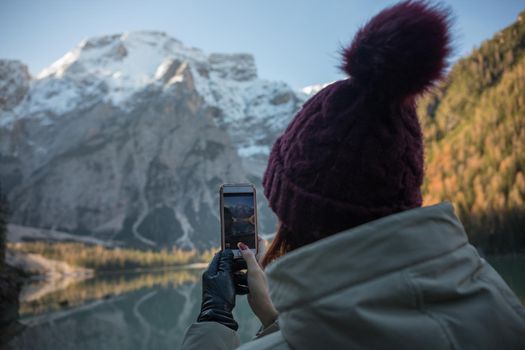 Dolomites nature. Lago di braies lake. Huge beautiful mountains. A woman in a purple hat taking a photo on the view. Wide shot